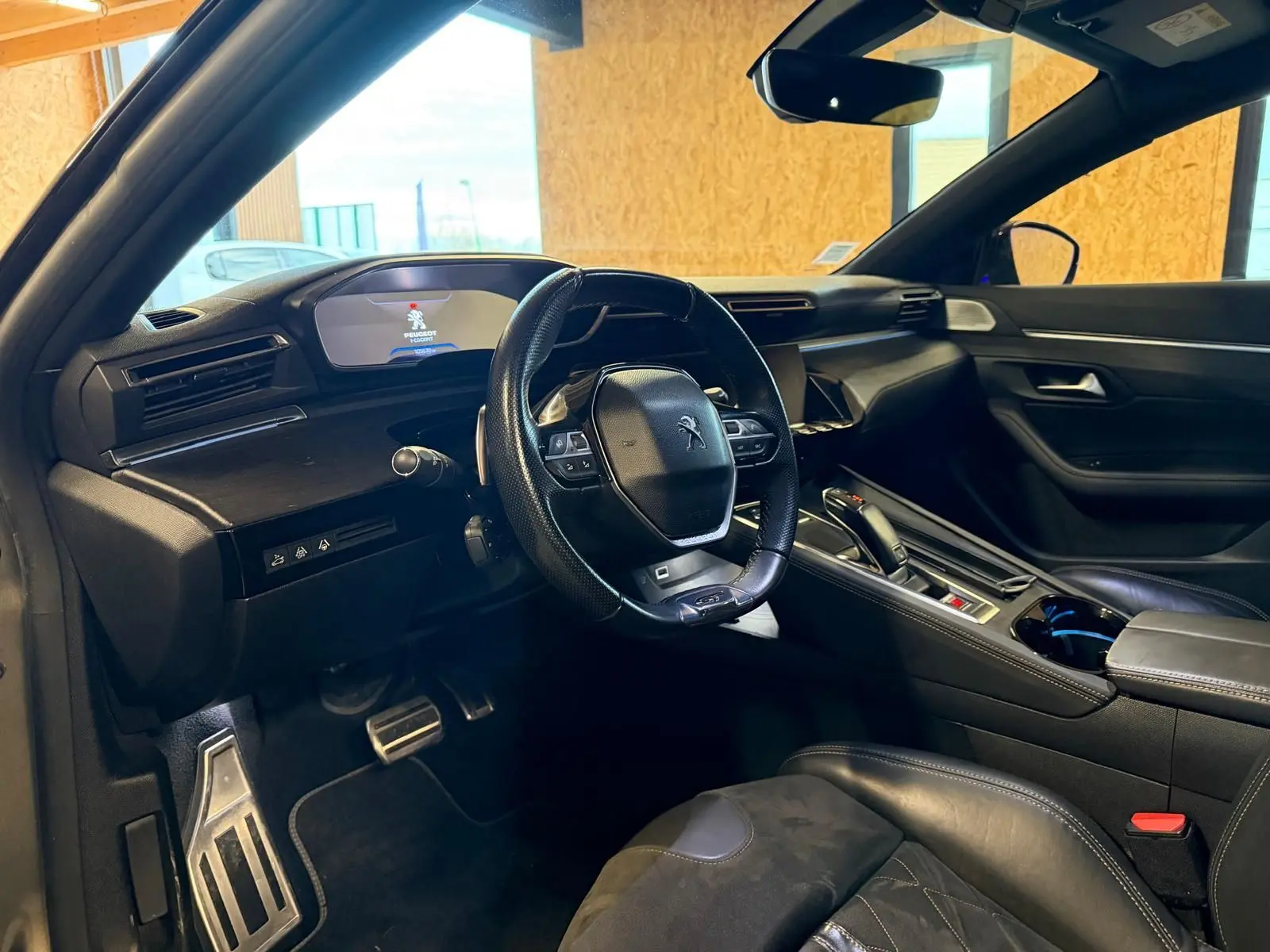 Intérieur Peugeot 508 gris, vue côté conducteur, volant cuir, tableau de bord avec écran numérique et inserts bois.