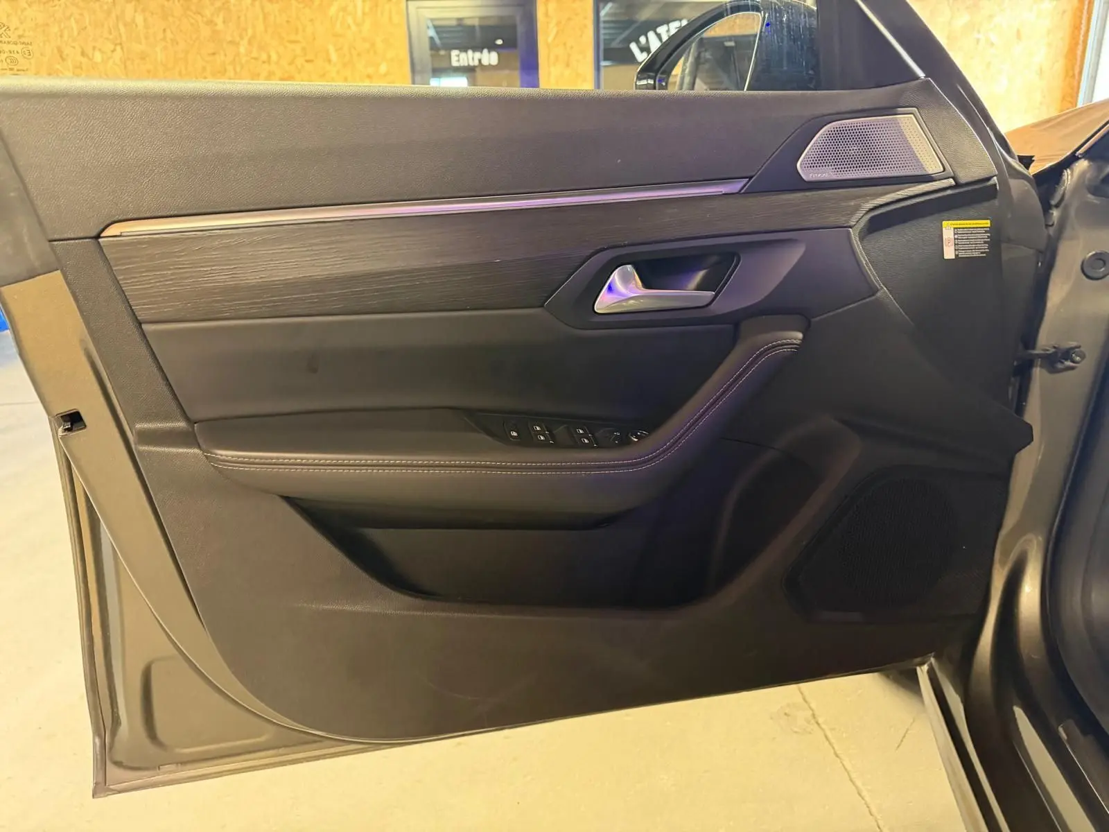 Vue intérieure côté gauche de la porte avant d’une Peugeot 508 gris, avec garniture noire et inserts bois.