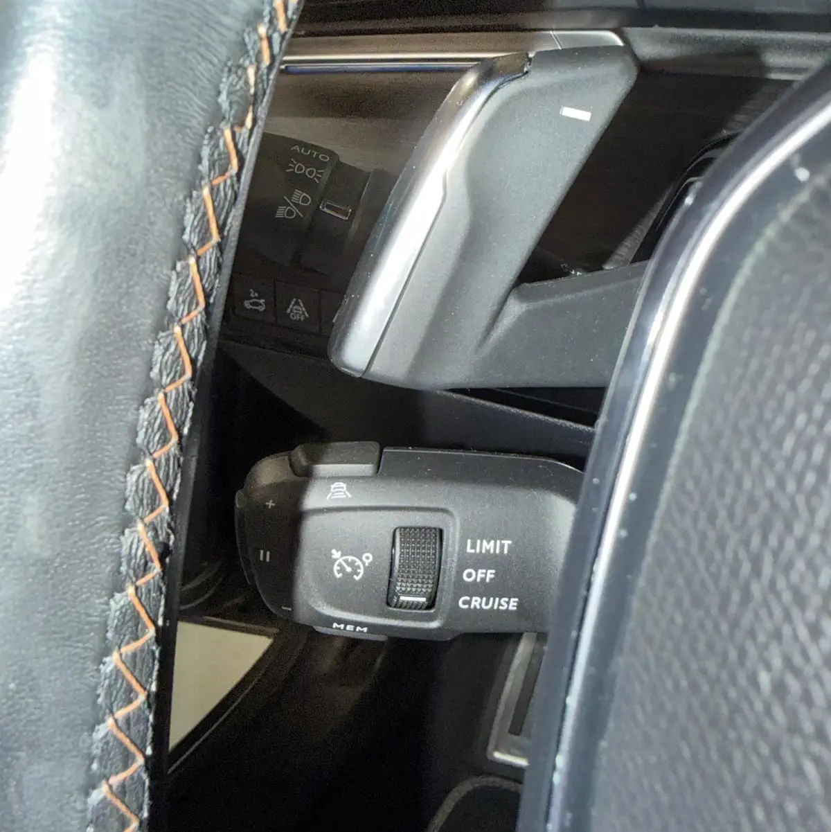 Gros plan sur la commande de régulateur de vitesse à gauche du volant cuir noir avec surpiqûres orange du Peugeot 508 gris.