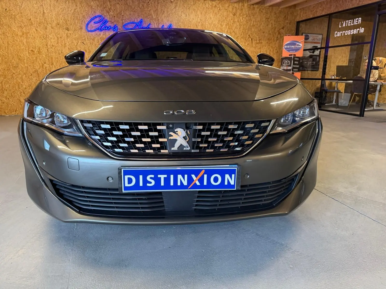 Vue frontale d'une Peugeot 508 gris métallisé avec calandre chromée et plaque Distinxion en intérieur d'atelier.