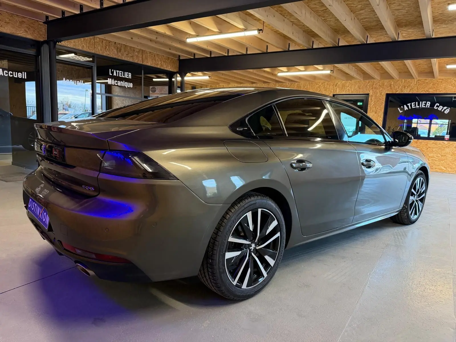 Vue 3/4 arrière droit d'une Peugeot 508 gris métallisé avec jantes alu et feux arrière LED, en intérieur showroom.