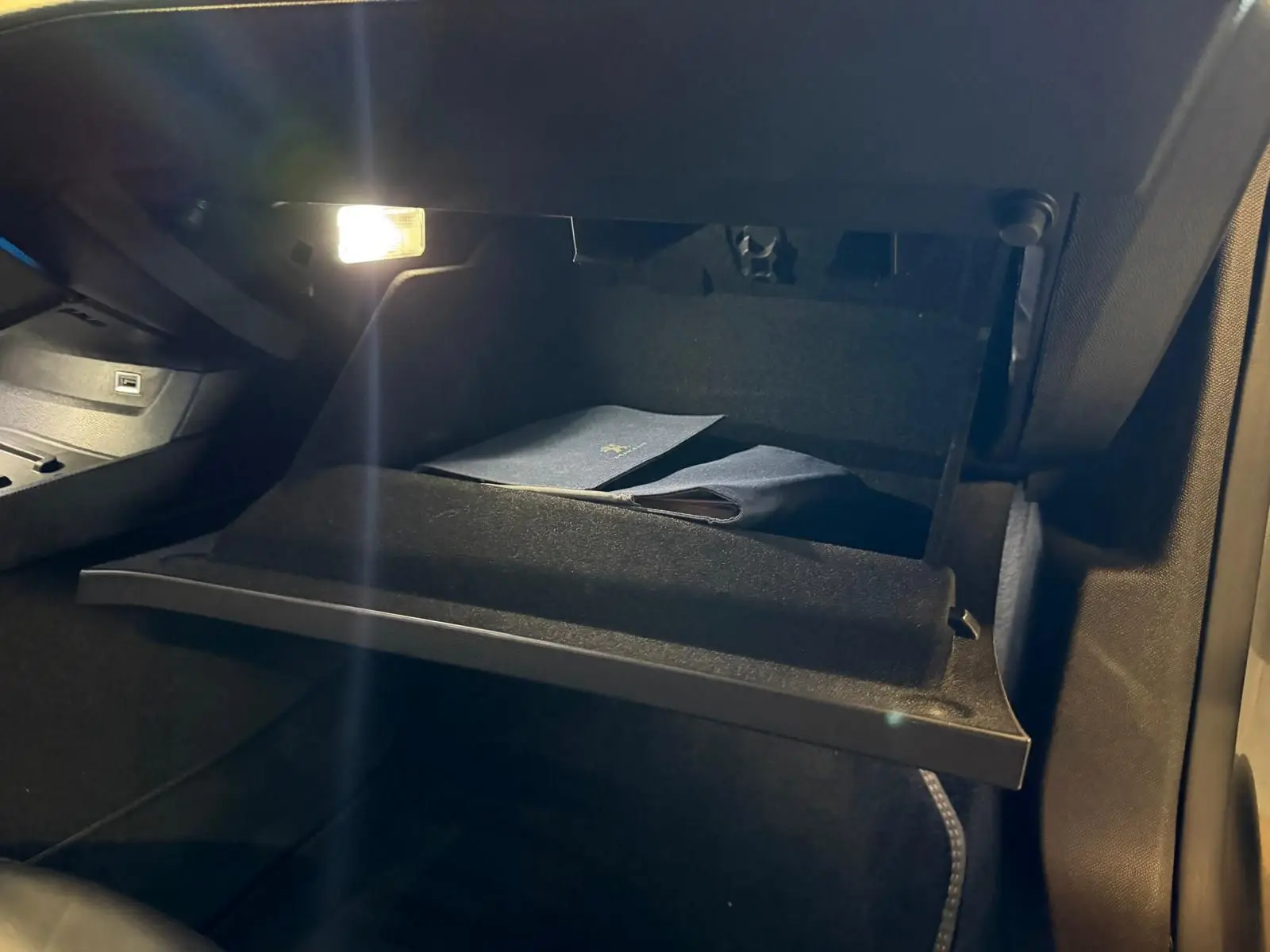 Gros plan sur la boîte à gants ouverte éclairée à l'intérieur de la Peugeot 508 gris, montrant des documents rangés.