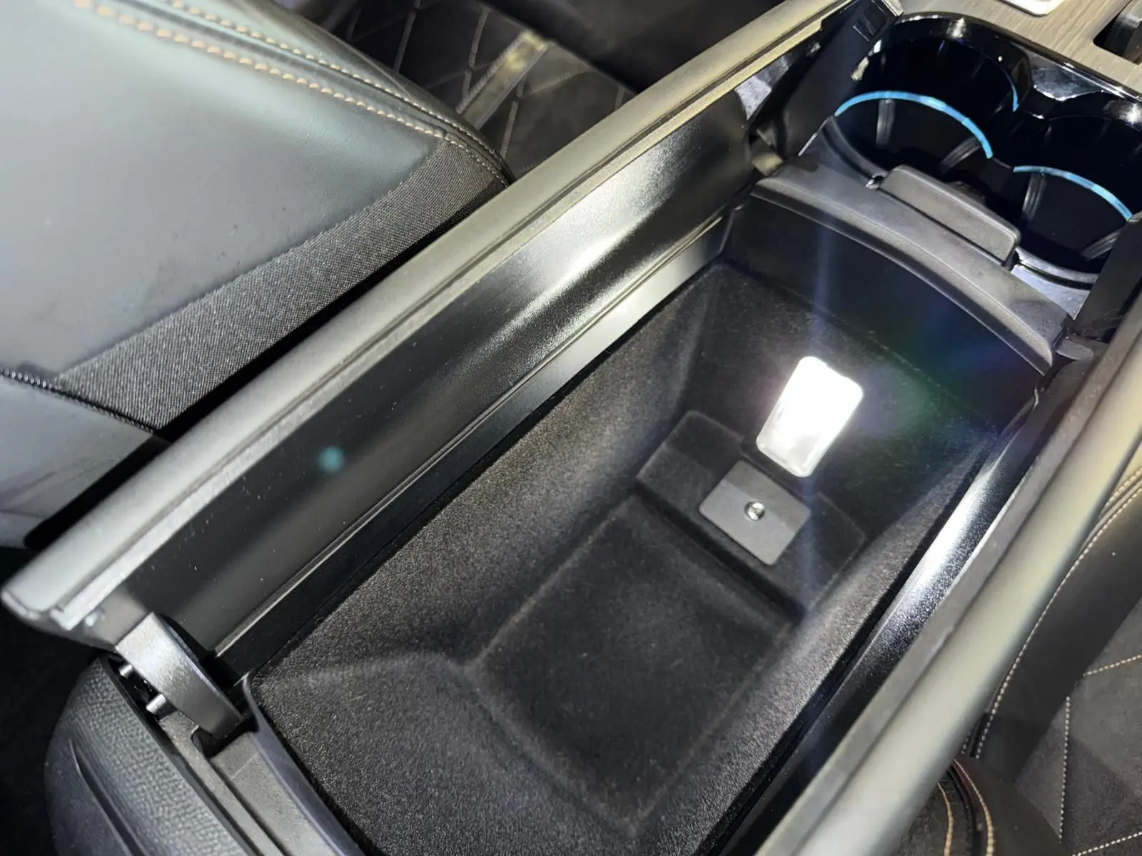 Vue rapprochée de l'accoudoir central ouvert en cuir noir de la Peugeot 508 II gris, avec compartiment de rangement éclairé.