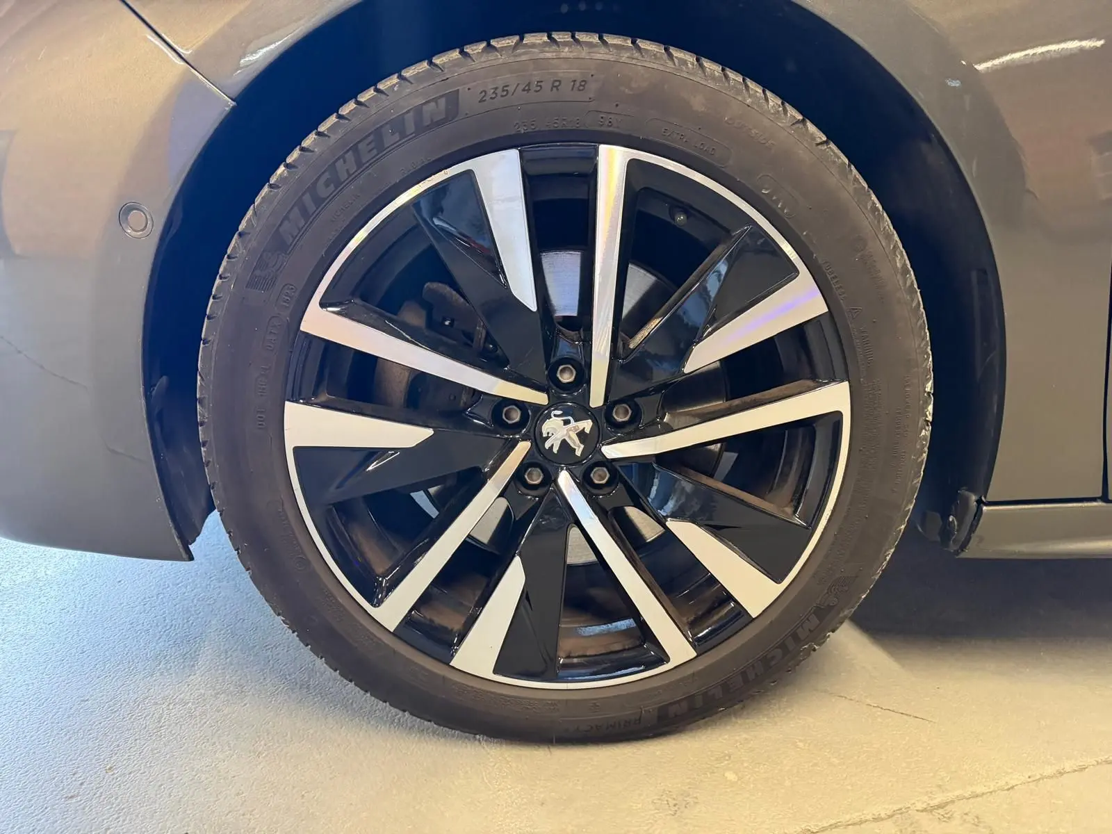 Gros plan sur la jante alu noire et argentée avec logo Peugeot centrale, sur roue avant droite d'une 508 gris 2019.