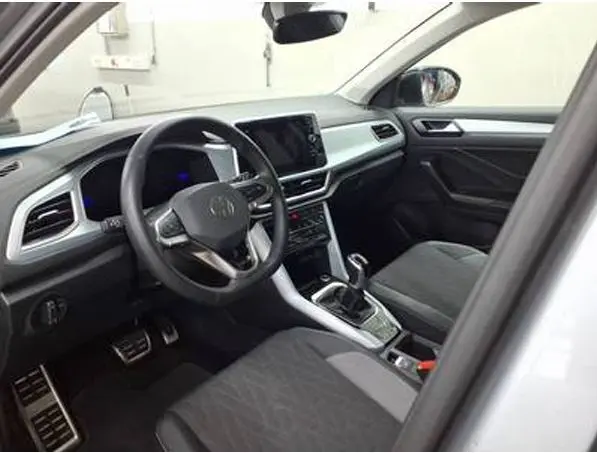 Vue intérieure côté conducteur du Volkswagen T-Roc gris clair 2025, avec tableau de bord moderne et sièges tissu noir.