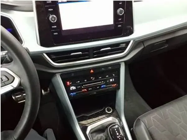 Vue intérieure centrée sur la console centrale et le levier de vitesse du Volkswagen T-Roc gris clair, avec écran tactile et commandes climatisation.