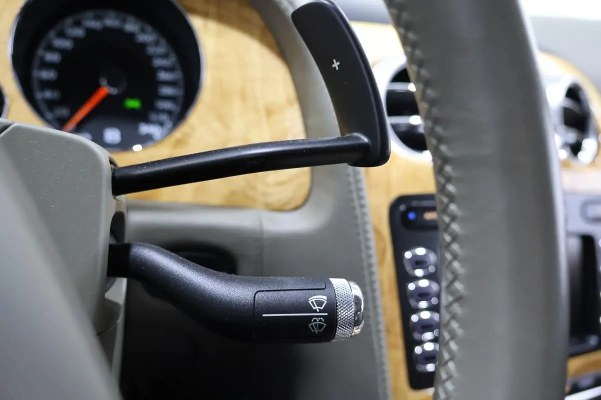 Gros plan sur la commande d’essuie-glace noire et volant cuir gris dans l’habitacle bois clair d’une Bentley Continental Flying Spur.