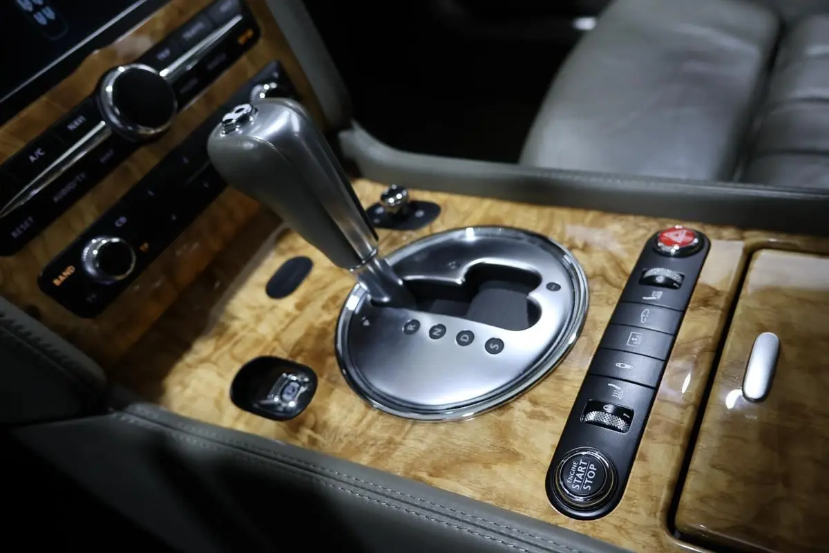 Gros plan sur la console centrale en bois clair de la Bentley Continental Flying Spur, avec levier de vitesse automatique et boutons de commande.
