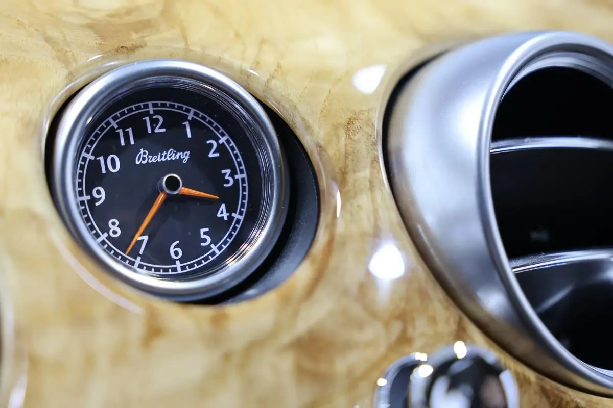 Gros plan sur l'horloge Breitling intégrée au tableau de bord en bois clair d'une Bentley Continental Flying Spur.