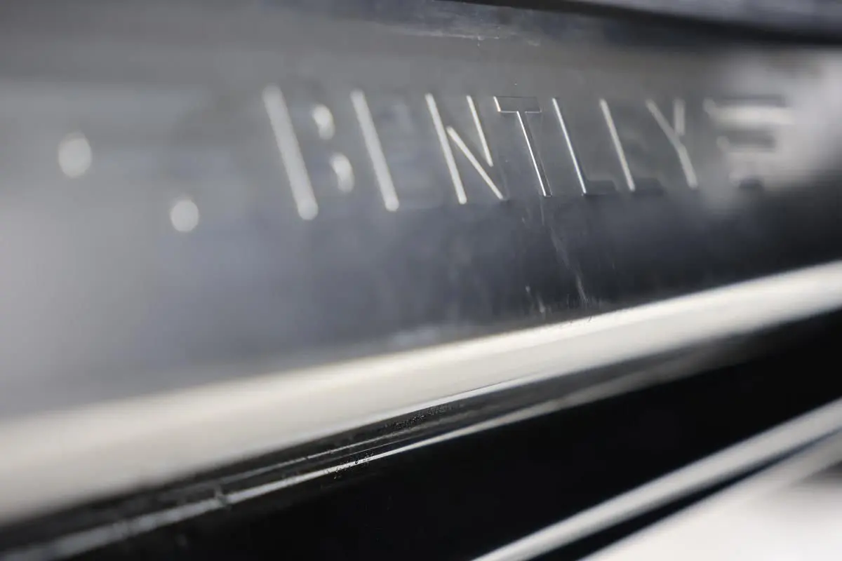 Gros plan sur la plaque de seuil de porte en métal gravé "BENTLEY" sur une Bentley Continental Flying Spur vert foncé.