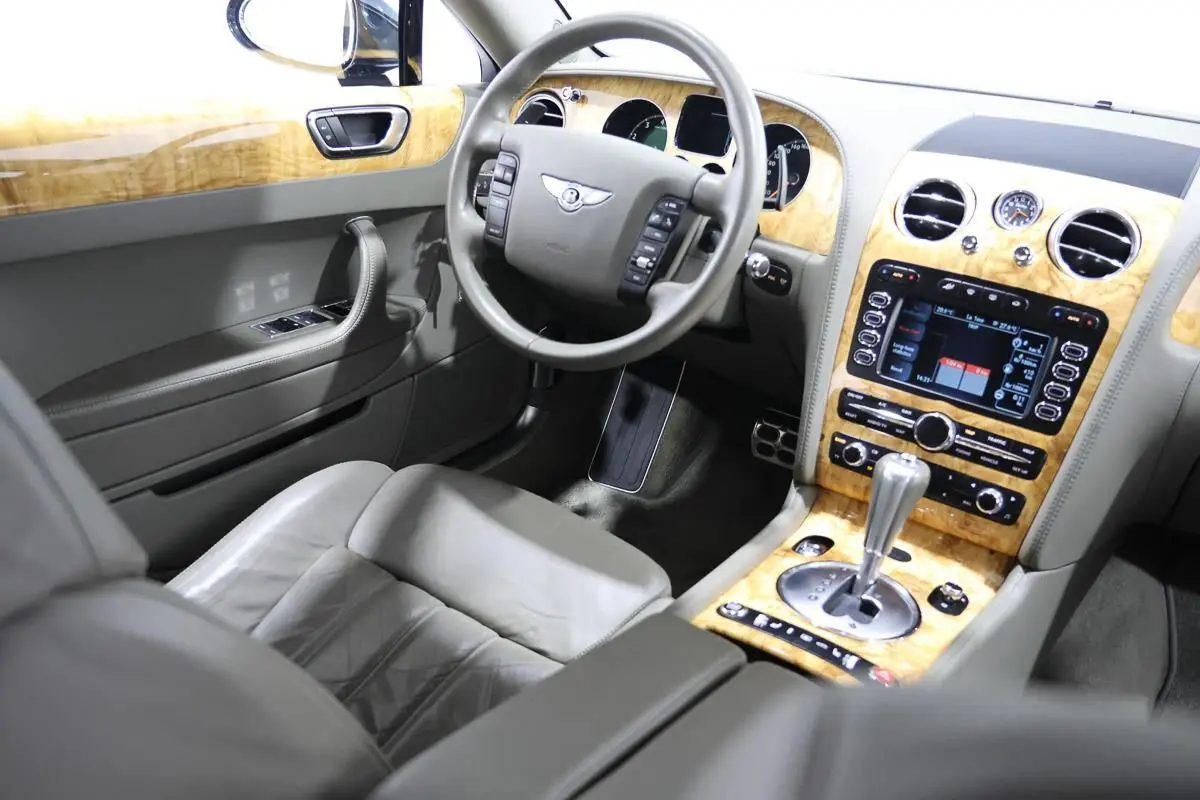 Vue intérieure côté conducteur de la Bentley Continental Flying Spur 2006 avec tableau de bord en bois clair et cuir gris.
