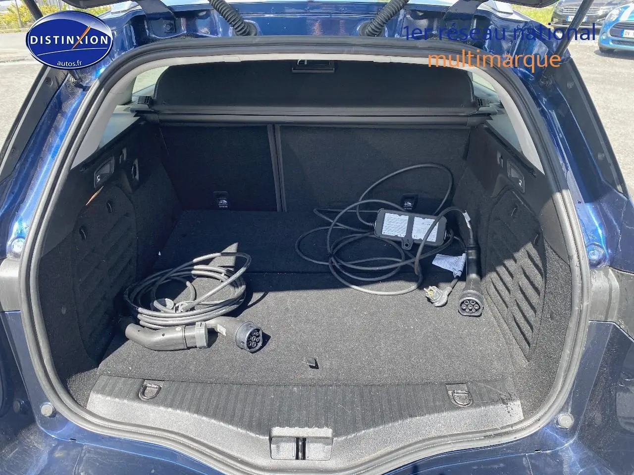Coffre ouvert en vue arrière d’une Renault Mégane IV Estate bleu avec câbles de recharge hybride visibles.