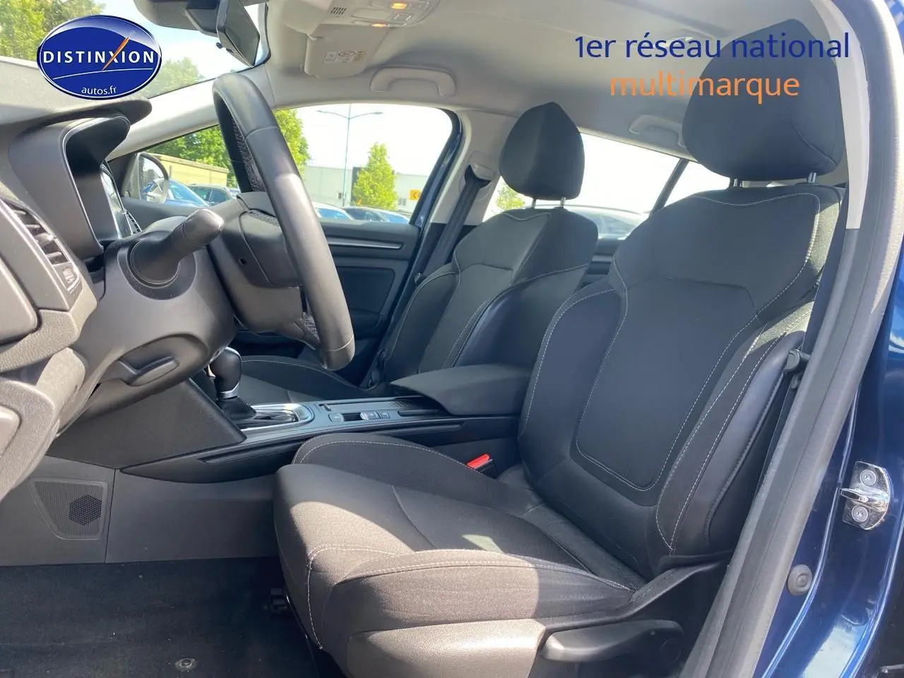 Vue intérieure côté gauche de la Renault Mégane IV Estate bleu, montrant les sièges avant en tissu gris foncé et la console centrale.