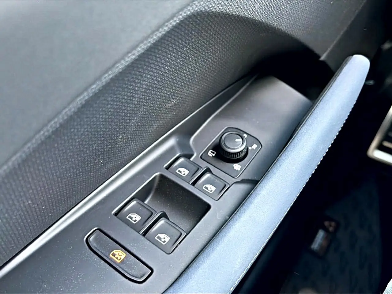 Gros plan sur la commande des vitres et rétroviseurs côté conducteur avec accoudoir bleu dans une CUPRA Terramar 2026.