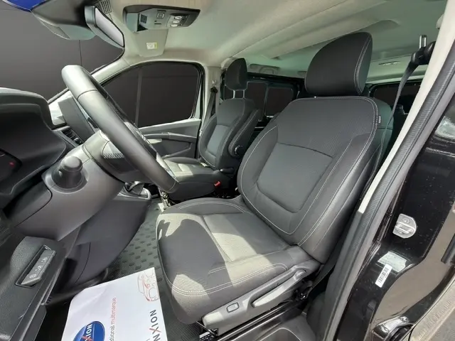 Vue intérieure côté conducteur du Nissan Primastar noir 2025, sièges en tissu gris et tableau de bord moderne.