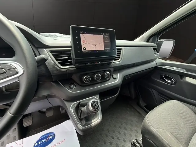 Vue intérieure côté conducteur du tableau de bord noir du Nissan Primastar 2025 avec écran tactile et levier de vitesses manuel.