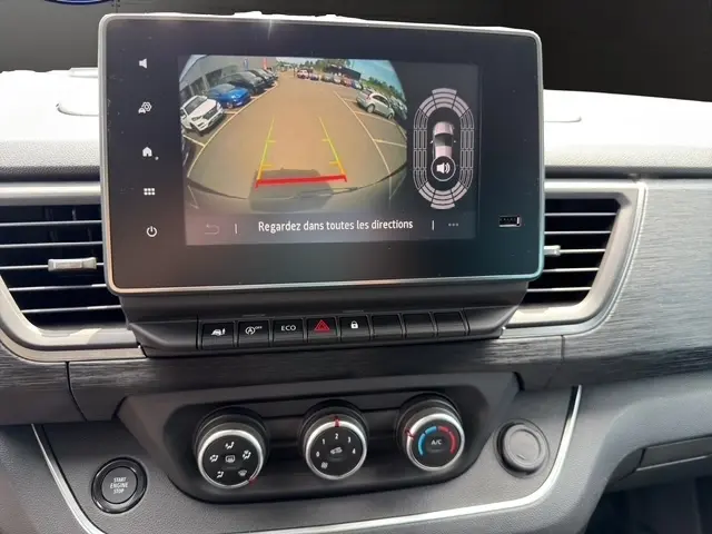 Écran tactile central montrant la caméra de recul d’un Nissan Primastar noir, avec commandes climatisation et bouton démarrage visibles.
