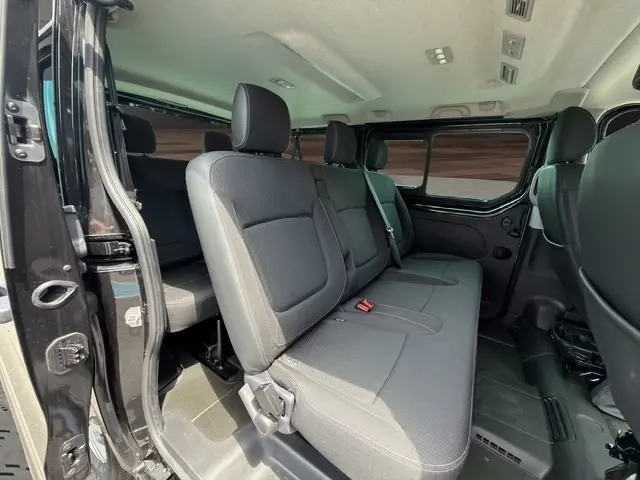 Vue intérieure côté gauche du Nissan Primastar noir 2025, montrant la banquette arrière et la porte latérale ouverte.