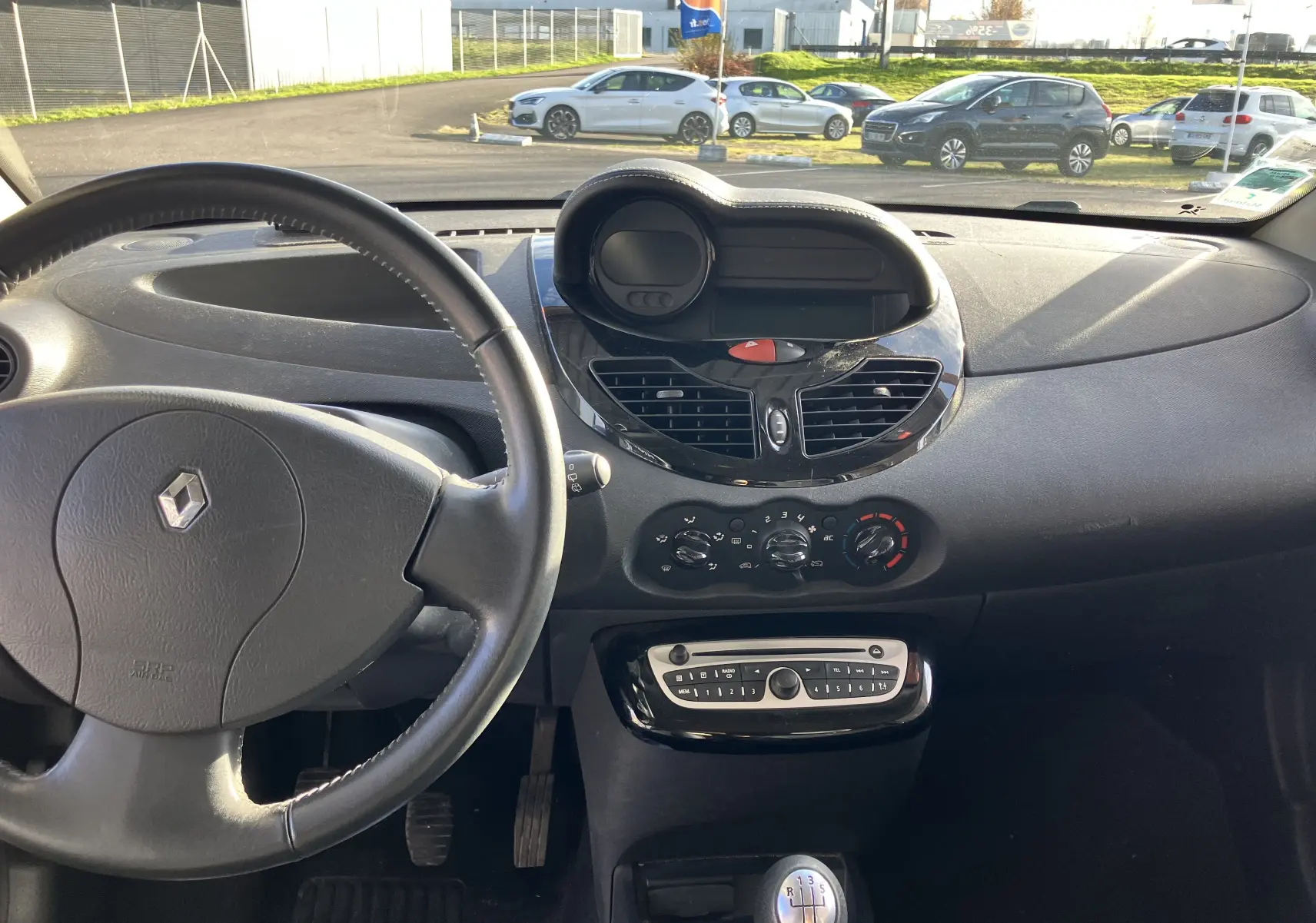 Vue intérieure du tableau de bord noir de la Renault Twingo II 75CH ESS 2011 avec volant et commandes centrales visibles.