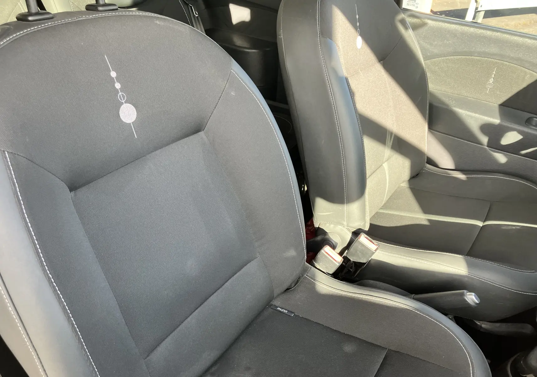 Vue rapprochée des sièges avant noirs de la Renault Twingo II 2011, montrant les détails de la sellerie et les ceintures de sécurité.