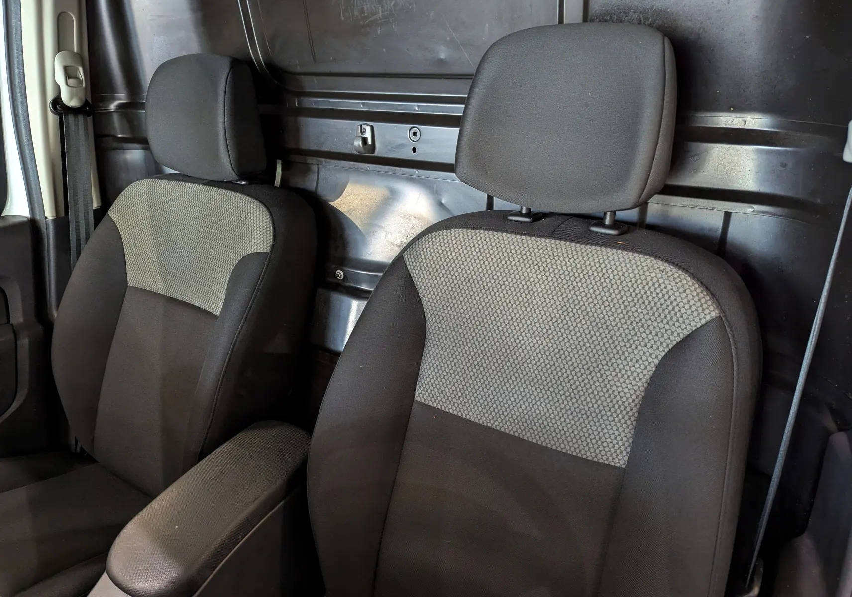 Gros plan sur les sièges avant en tissu gris et noir du Renault Kangoo Express blanc, avec cloison métallique arrière visible.
