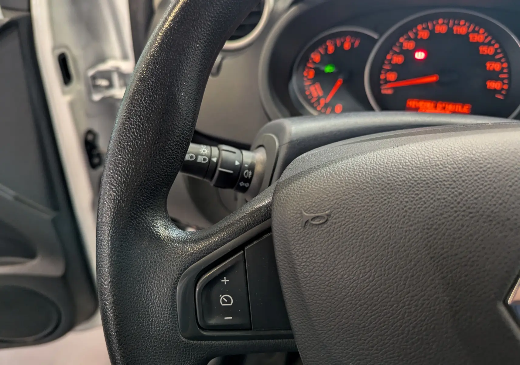 Gros plan sur le volant noir et le tableau de bord éclairé du Renault Kangoo Express blanc, côté conducteur ouvert.