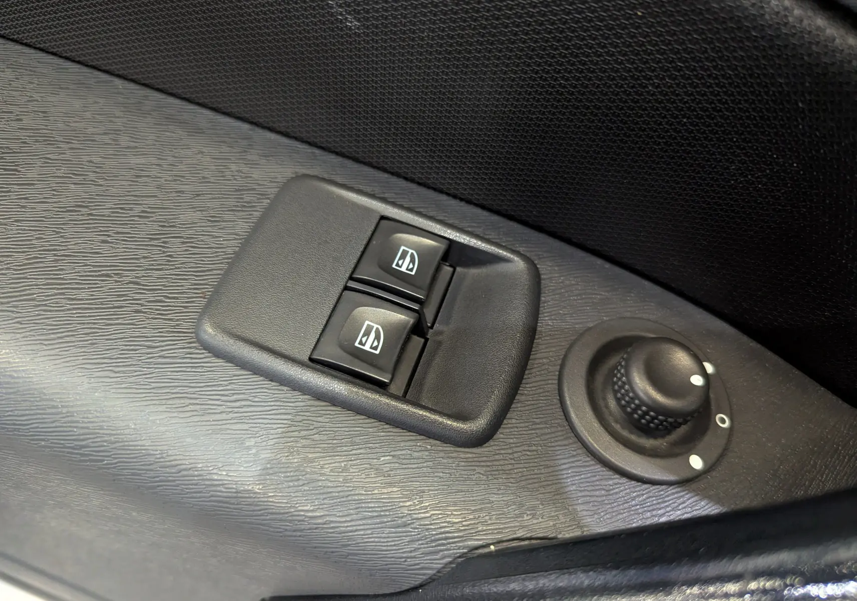 Gros plan sur les commandes des vitres électriques et le réglage des rétroviseurs côté conducteur du Renault Kangoo Express blanc.