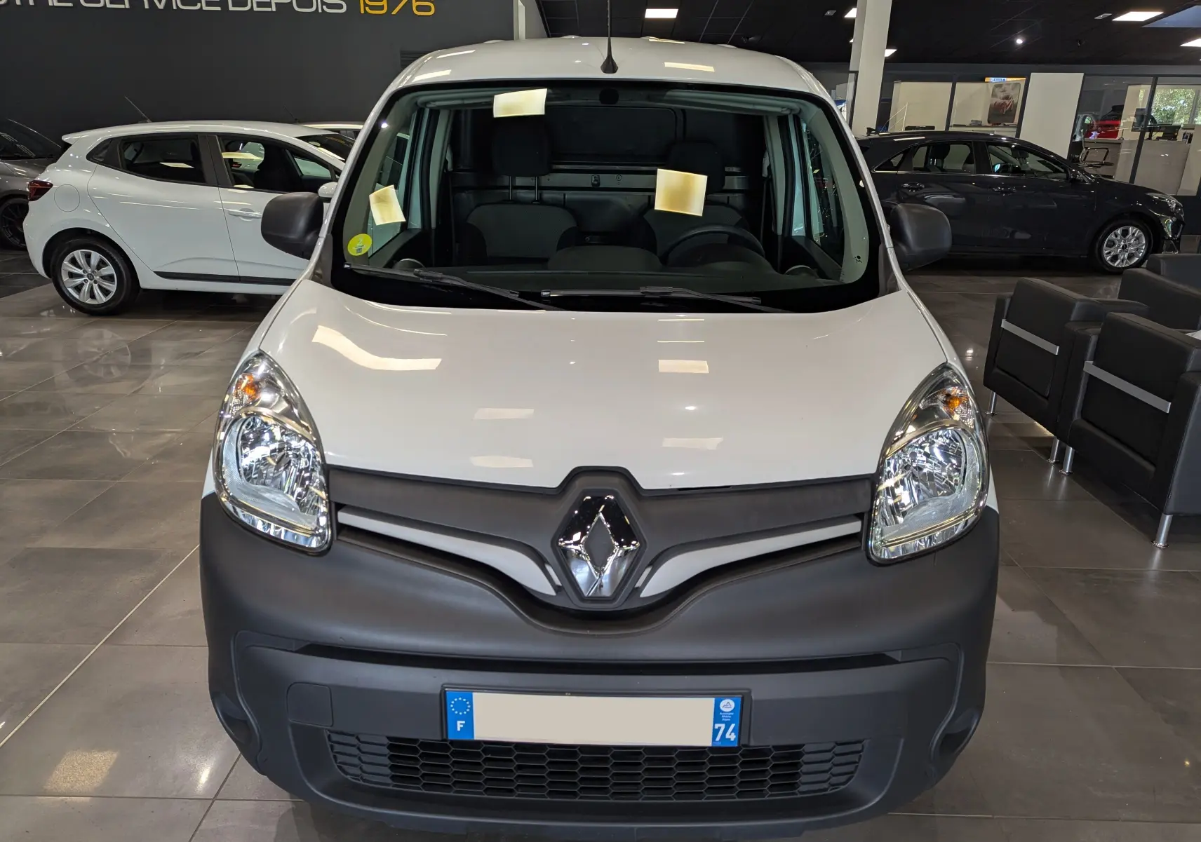 Vue frontale d'un Renault Kangoo Express blanc minéral avec pare-chocs noir mat dans un showroom.