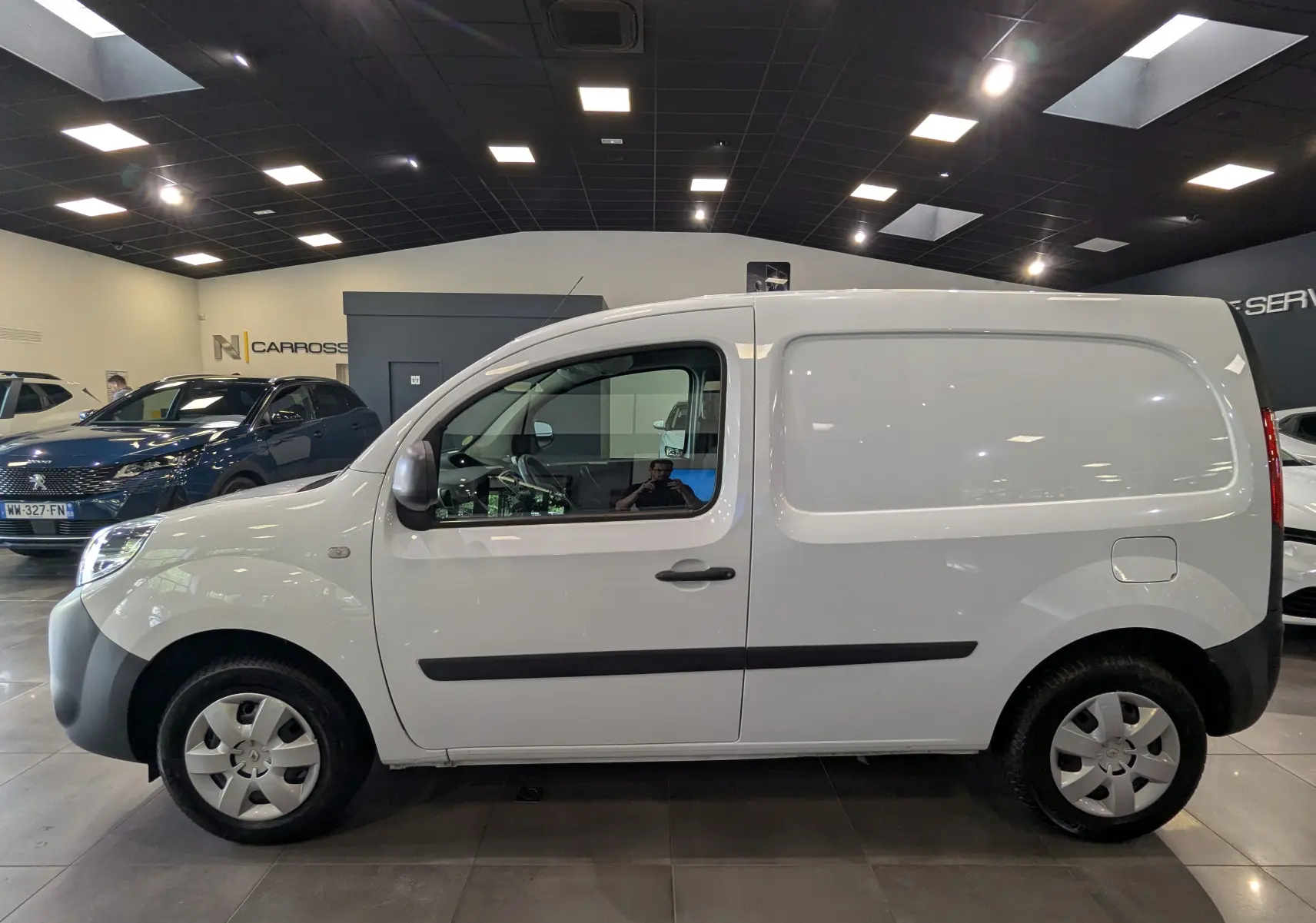 Profil côté gauche d'un Renault Kangoo Express blanc minéral, version utilitaire, dans un showroom lumineux.