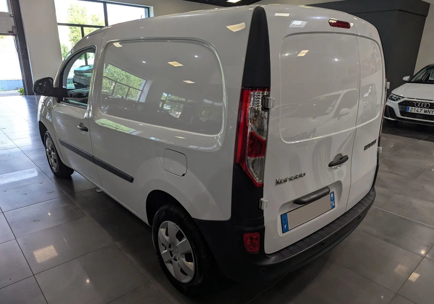 Vue 3/4 arrière droite d'un Renault Kangoo Express blanc minéral, fourgon utilitaire en showroom avec feux arrière verticaux.