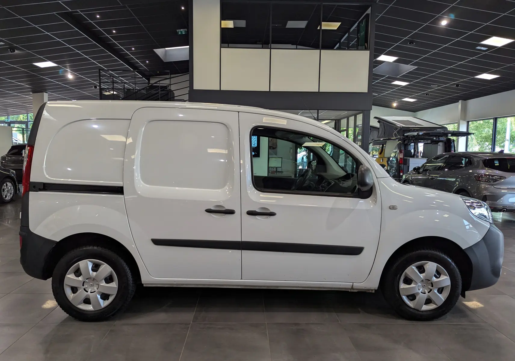 Profil côté droit d'un Renault Kangoo Express blanc minéral, version utilitaire avec portes latérales pleines, en intérieur showroom.