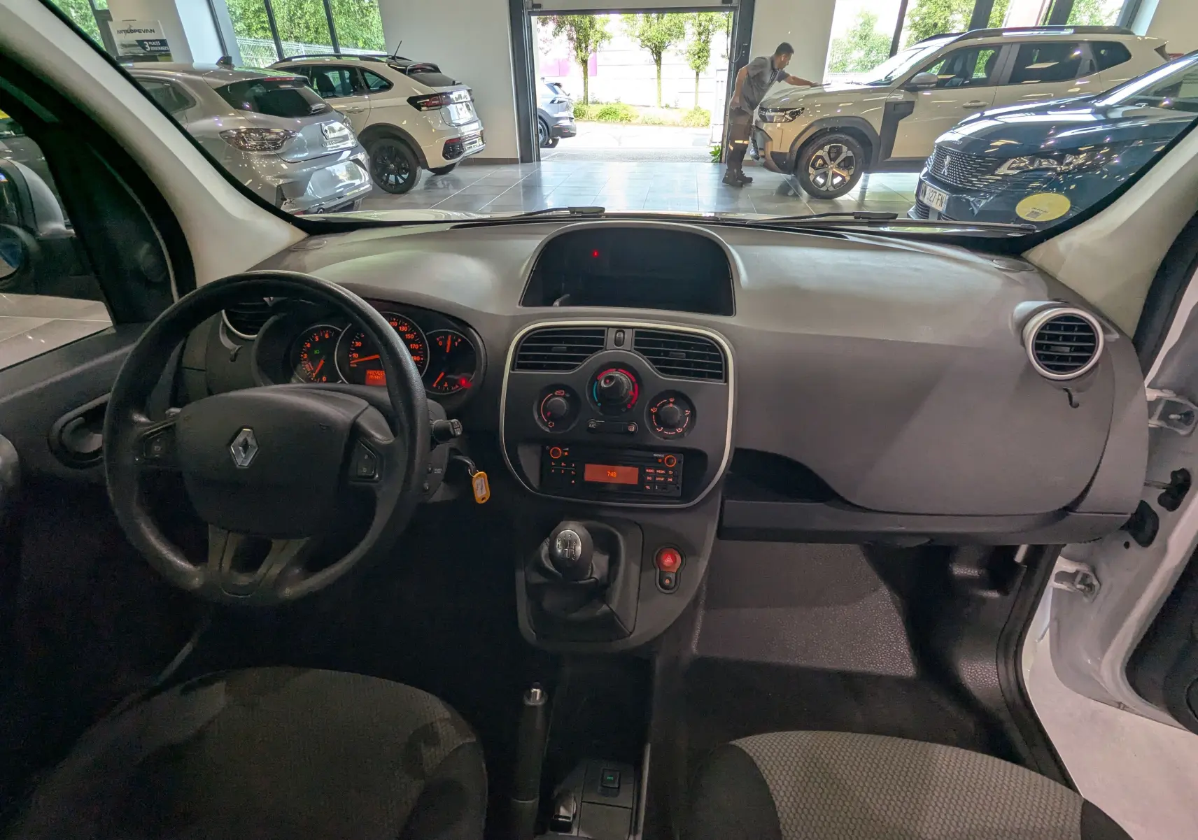 Vue intérieure avant du Renault Kangoo Express blanc minéral 2021, tableau de bord simple avec volant Renault et levier de vitesses manuel.