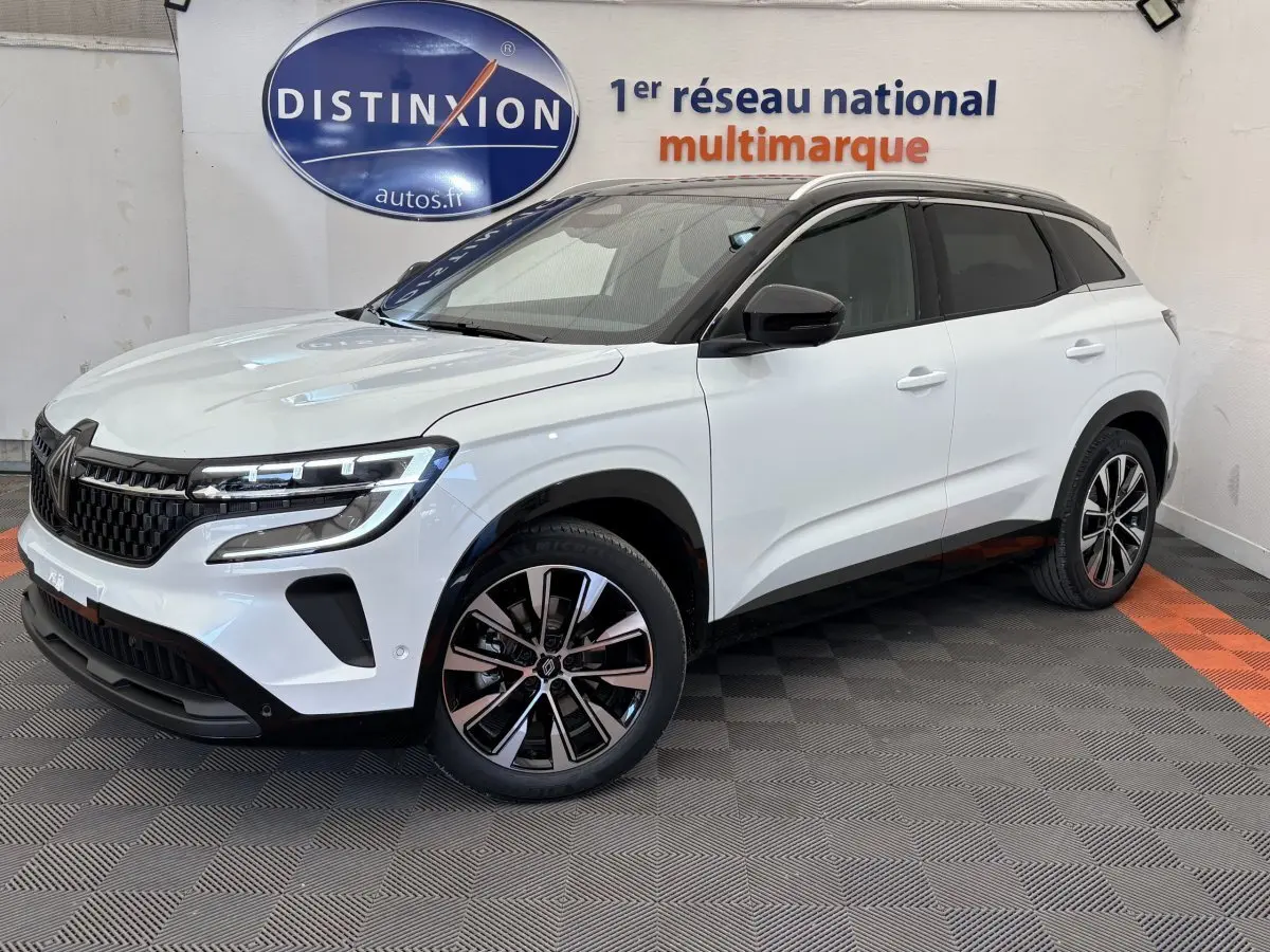 Vue 3/4 avant droite du Renault Austral blanc avec jantes alliage et toit noir dans un showroom multimarque.