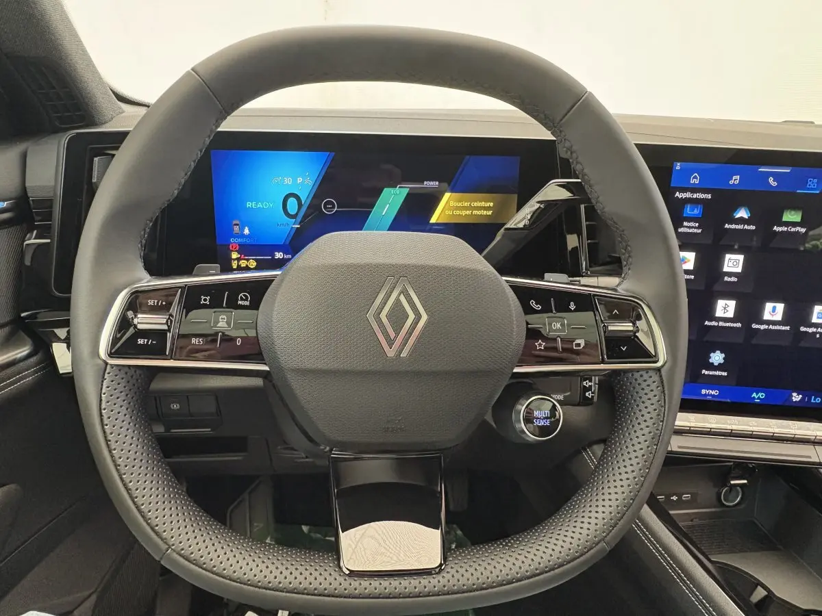 Vue frontale du volant cuir perforé et des écrans numériques du tableau de bord du Renault Austral blanc hybride 2025.