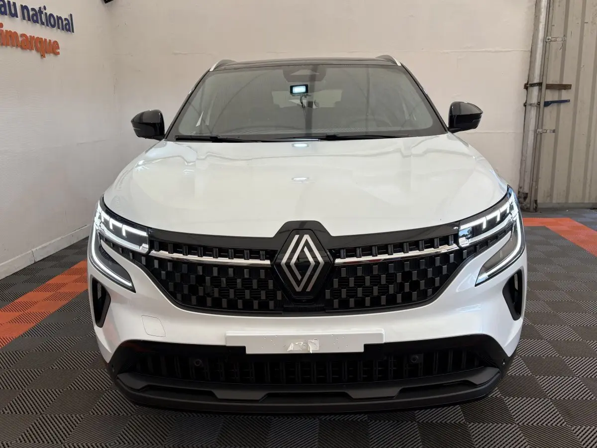 Vue frontale d'un Renault Austral blanc avec calandre noire et feux LED allumés dans un showroom.