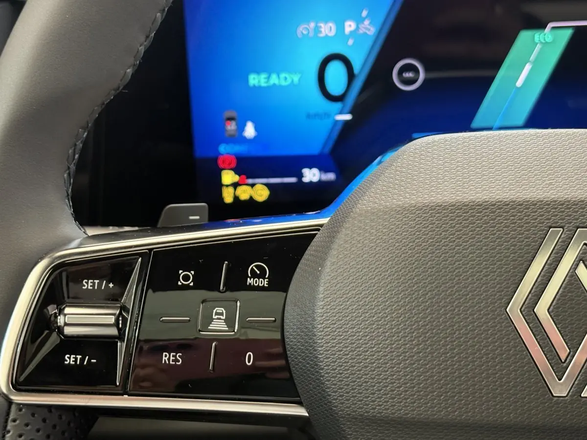 Gros plan sur le volant gris du Renault Austral 2025 avec commandes multifonctions et tableau de bord numérique bleu en arrière-plan.