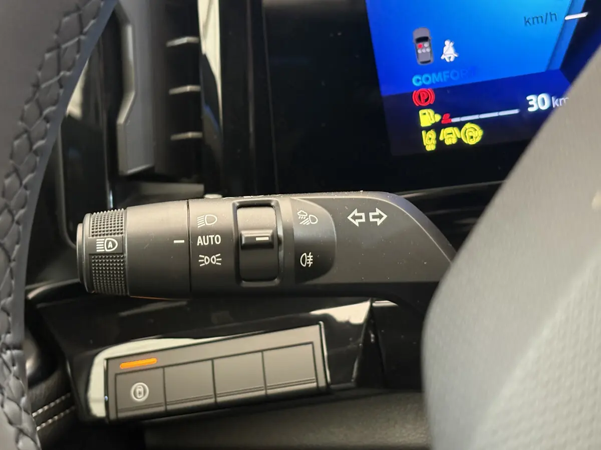 Gros plan sur la commande des feux et clignotants à gauche du volant dans le tableau de bord noir du Renault Austral blanc.