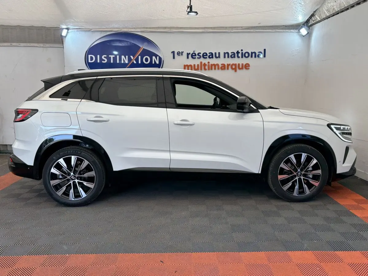 Profil côté gauche du Renault Austral blanc hybride 2025 avec jantes alliage et toit noir contrasté en intérieur showroom.