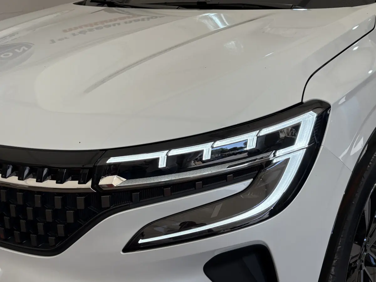 Gros plan sur le phare avant droit allumé du Renault Austral blanc, soulignant la calandre noire et les lignes modernes du capot.