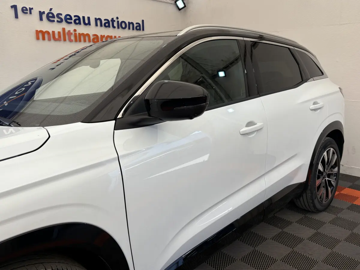 Profil côté gauche du Renault Austral blanc avec toit noir et rétroviseur noir dans un showroom.