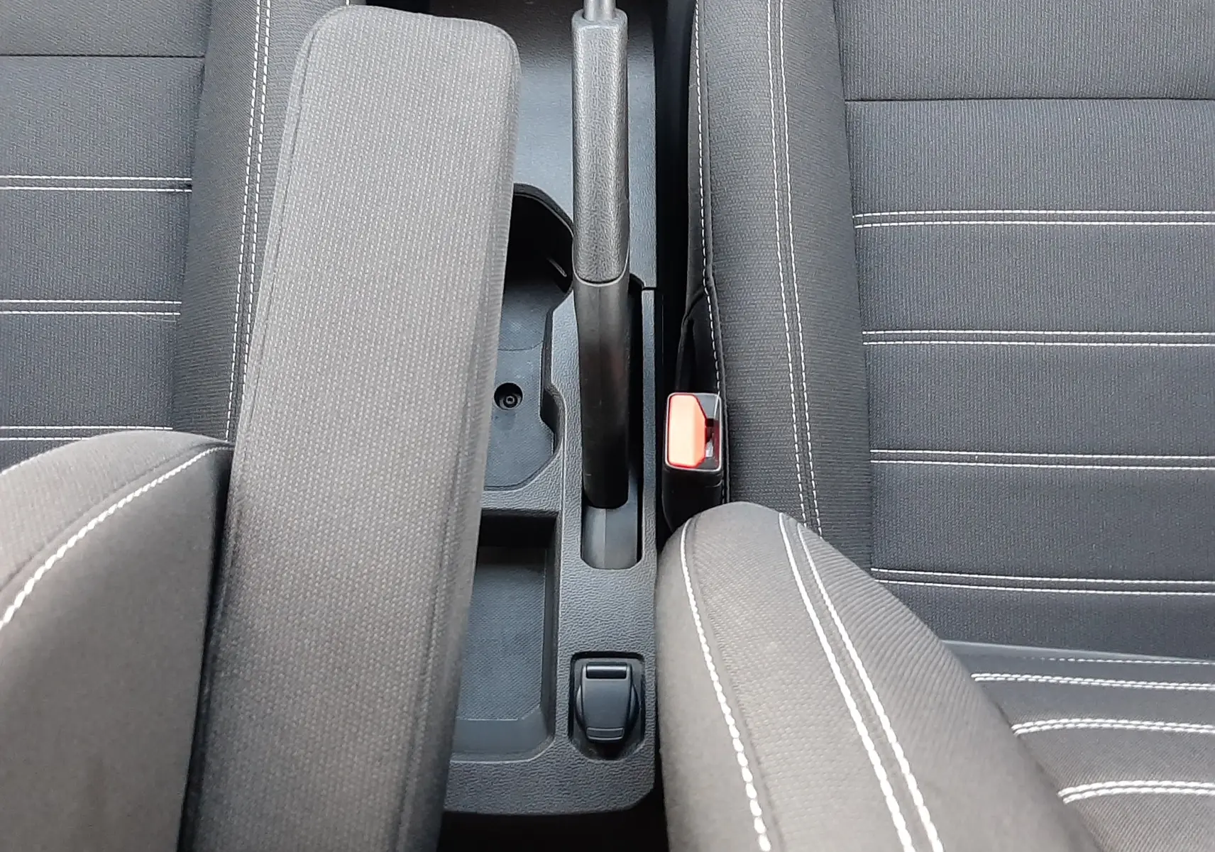 Vue plongeante sur l'accoudoir central et les sièges en tissu noir avec surpiqûres blanches du Dacia Jogger 2025.