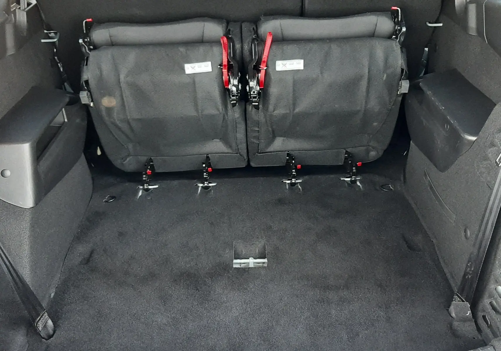 Vue arrière du coffre du Dacia Jogger 2025, sièges rabattus en tissu noir avec sangles rouges visibles.