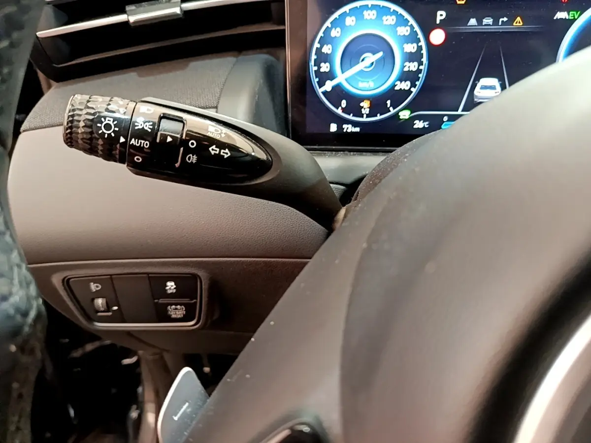 Gros plan sur la manette de clignotants et le tableau de bord numérique bleu du Hyundai Tucson 1.6 Hybrid 230 Creative.