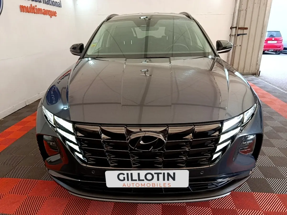 Vue avant d'un Hyundai Tucson gris foncé 2022 avec calandre noire et phares LED allumés dans un garage.