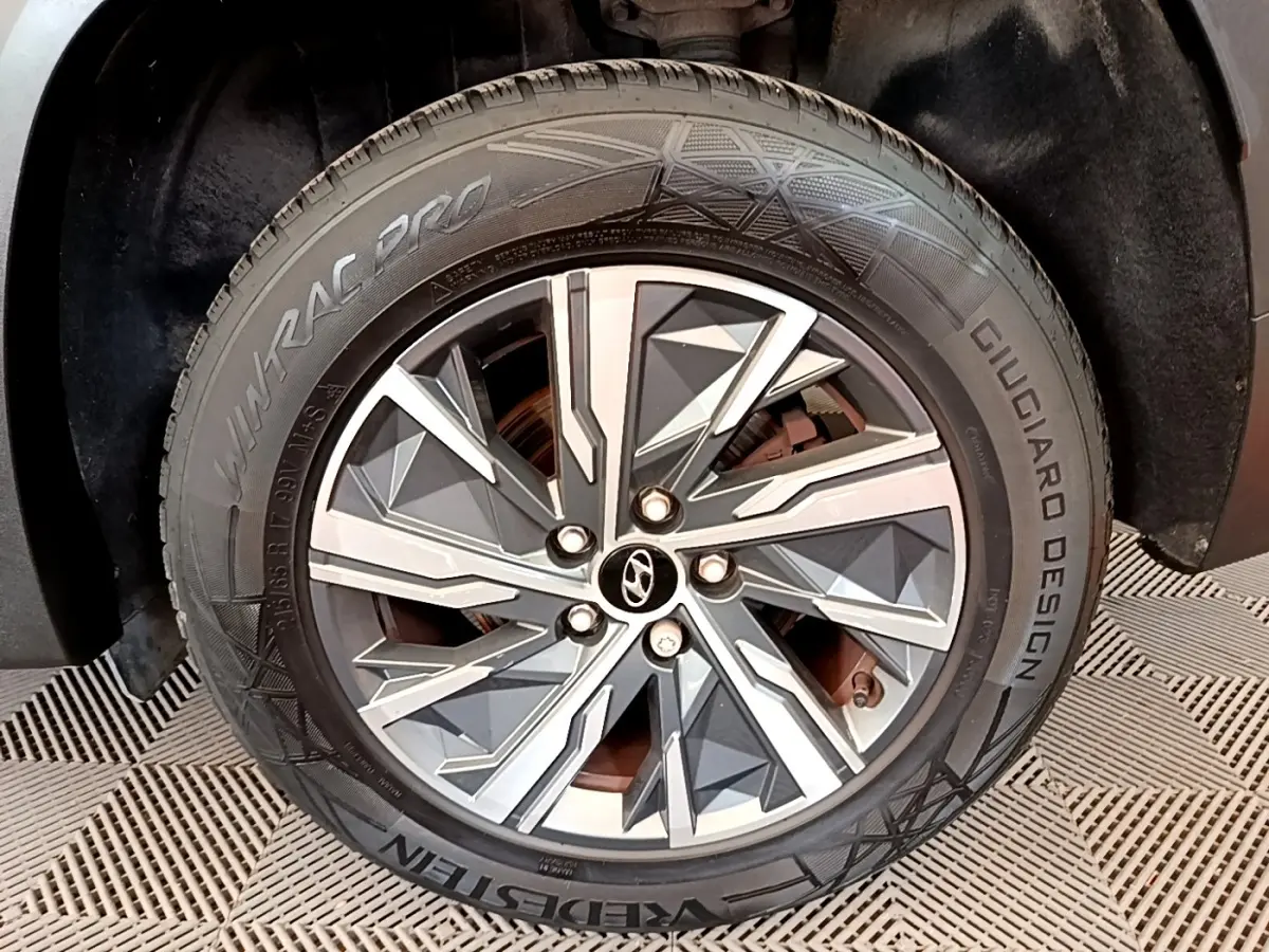 Gros plan sur la roue avant droite du Hyundai Tucson gris foncé, mettant en valeur la jante alu au design géométrique.