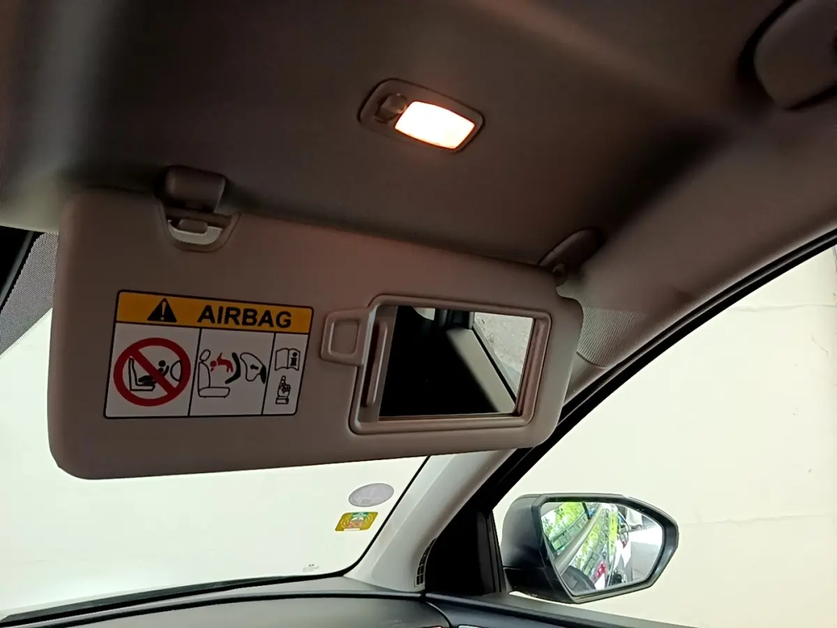 Détail intérieur montrant le pare-soleil côté conducteur avec miroir et avertissement airbag, rétro extérieur visible.