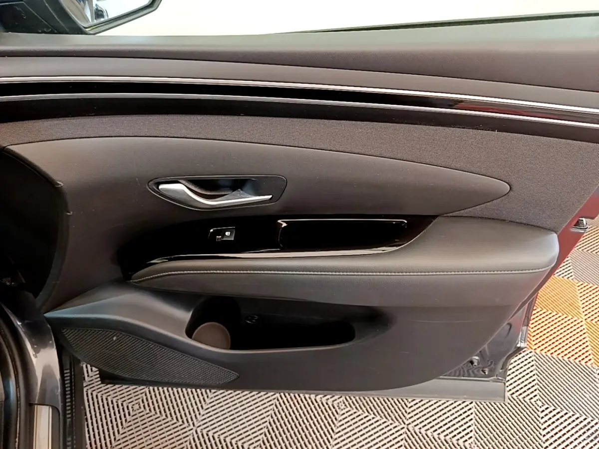 Vue intérieure sur la porte avant gauche d’un Hyundai Tucson gris foncé, avec poignée argentée et accoudoir noir.