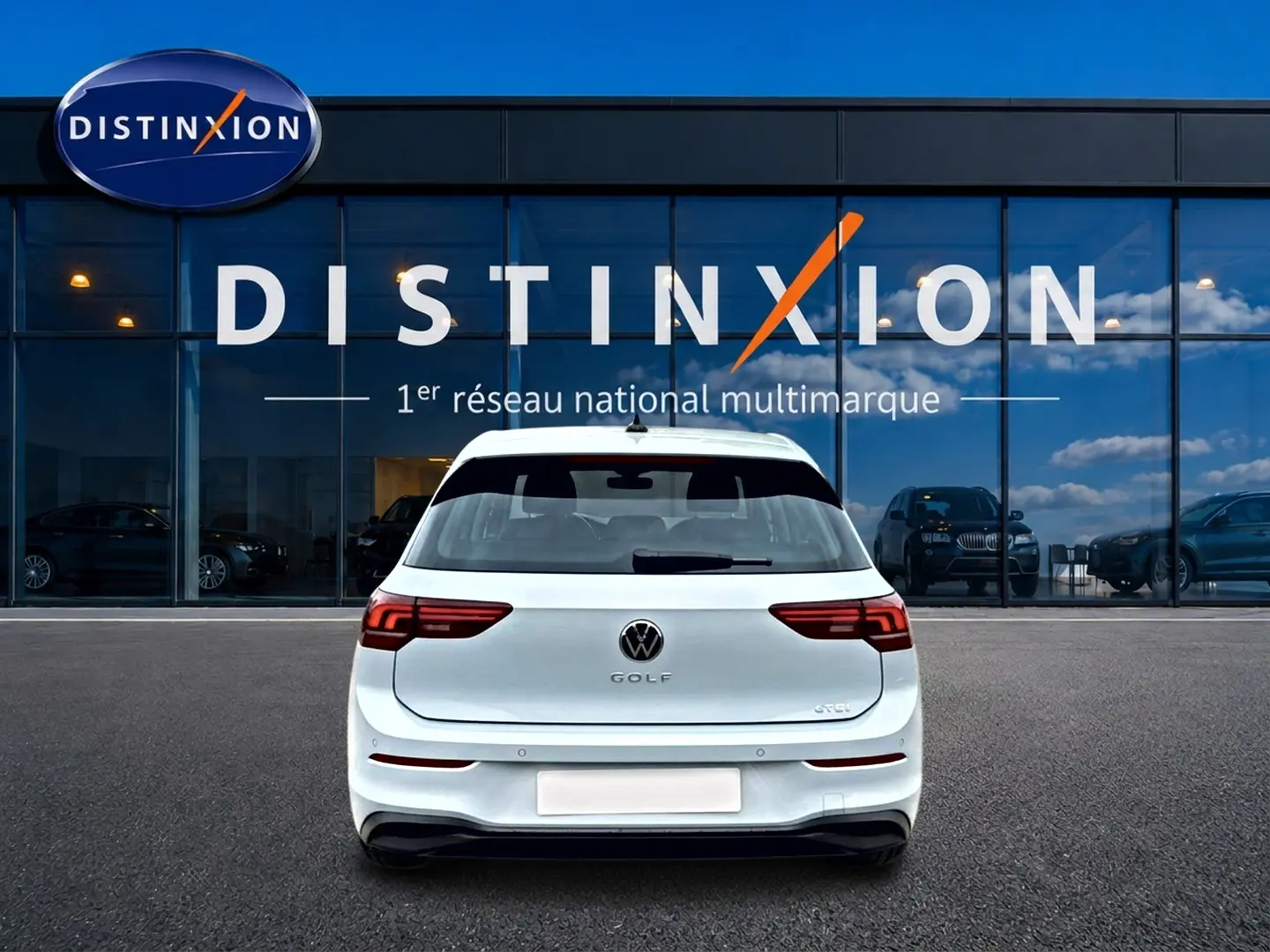 Vue arrière d'une Volkswagen Golf blanche garée devant une vitrine avec le logo Distinxion.