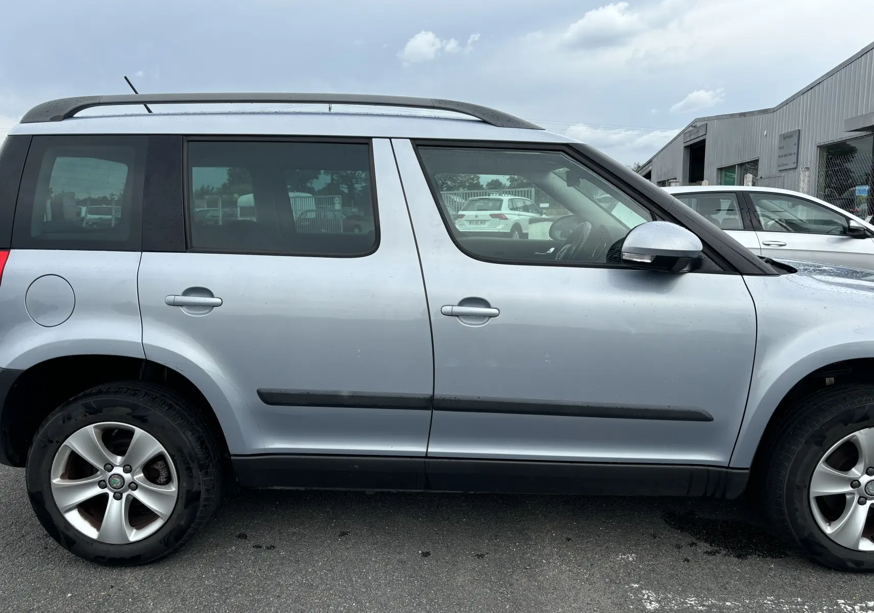 Profil côté droit d'un Skoda Yeti gris de 2012 avec barres de toit et jantes alliage visibles.