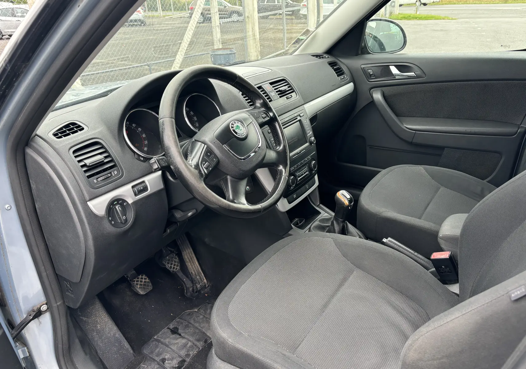 Intérieur côté conducteur du Skoda Yeti gris 2012, montrant le volant, tableau de bord et sièges en tissu noir.